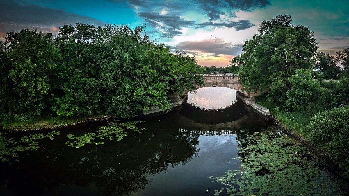 A Minneapolis stone bridge over a lily-pad lake at sunset.